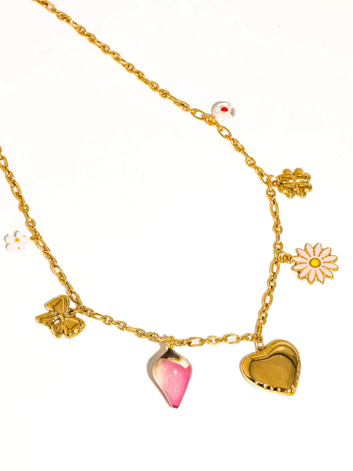 Gold-tone chain necklace with charms: pink enamel teardrop, gold heart, pink-daisy bloom, four-leaf clover, white bloom.