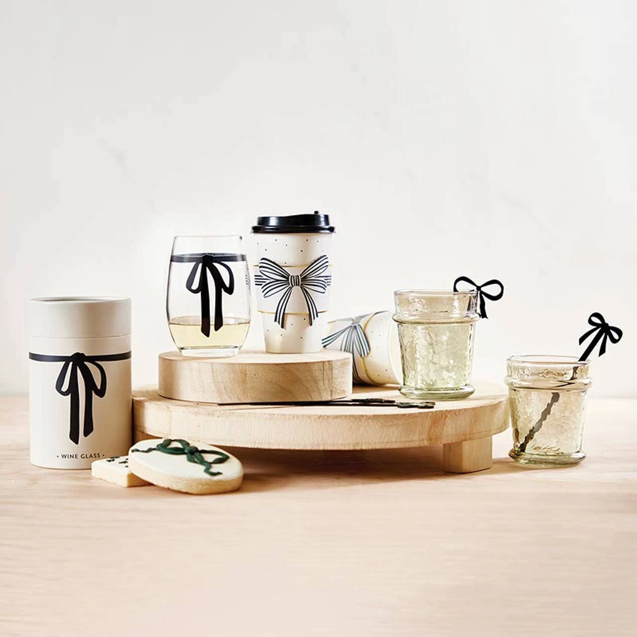 Clear stemless wine glass with a bold black bow motif, on a wooden display with a gift box and bow-tied glasses.
