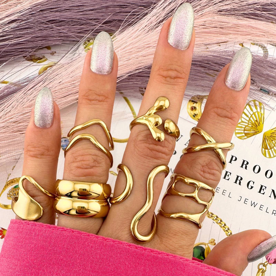Gold-tone rings on a hand with pink glitter nails: a wavy open band, a snake ring, and chunky curved bands, 18K gold plated stainless steel.