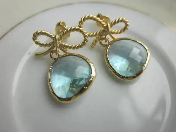 Gold-tone drop earrings with faceted aquamarine blue teardrop stones in rounded bezels, twisted rope bow accents