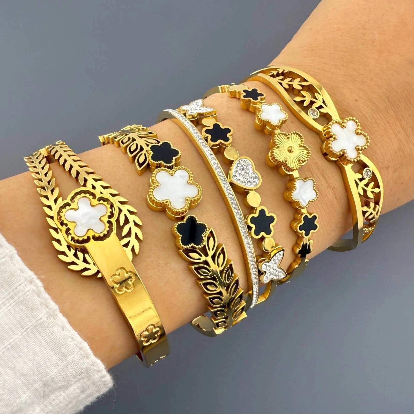 Stacked gold-tone bracelets, 18K gold-plated stainless steel, featuring white and black enamel flowers with crystal accents.