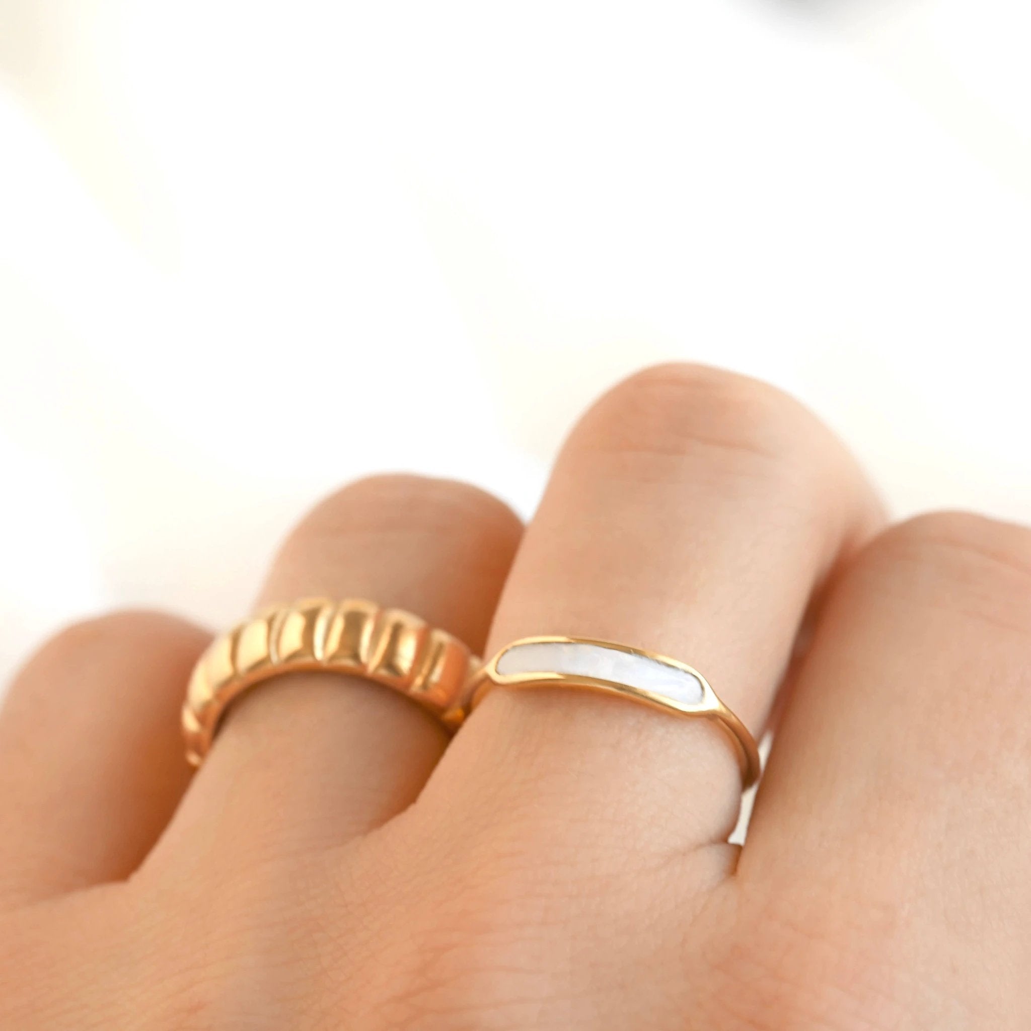 Thin gold Pearl Stacker ring with curved iridescent mother-of-pearl inlay, shown on finger beside a textured gold band.