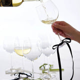 Six black velvet bow wine charms tied to wine glass stems, with a bottle pouring white wine into a glass in the background.