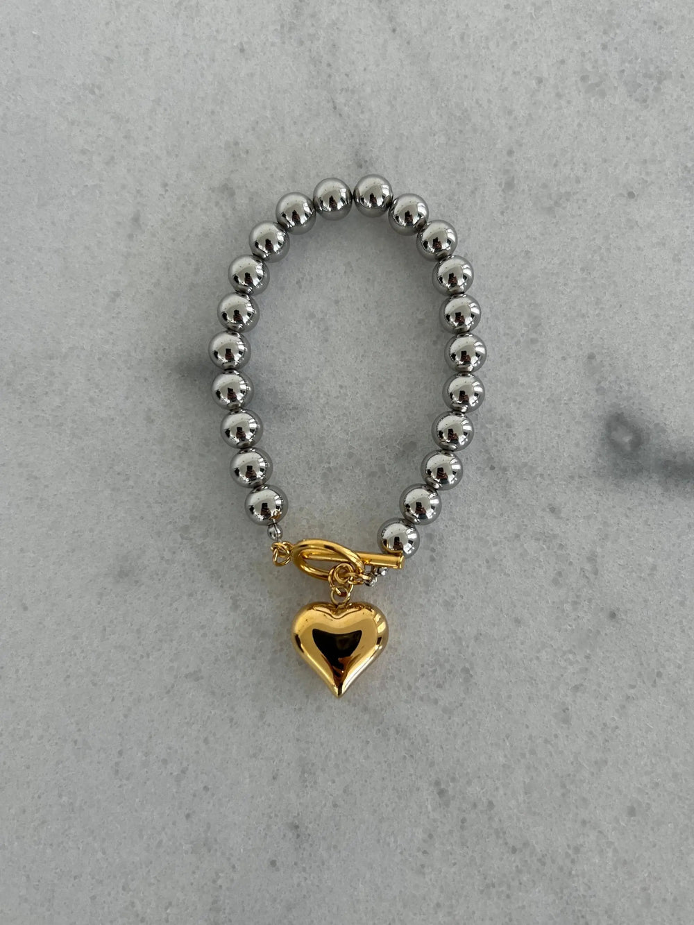 Silver-tone beaded bracelet with round beads and a gold heart charm pendant.