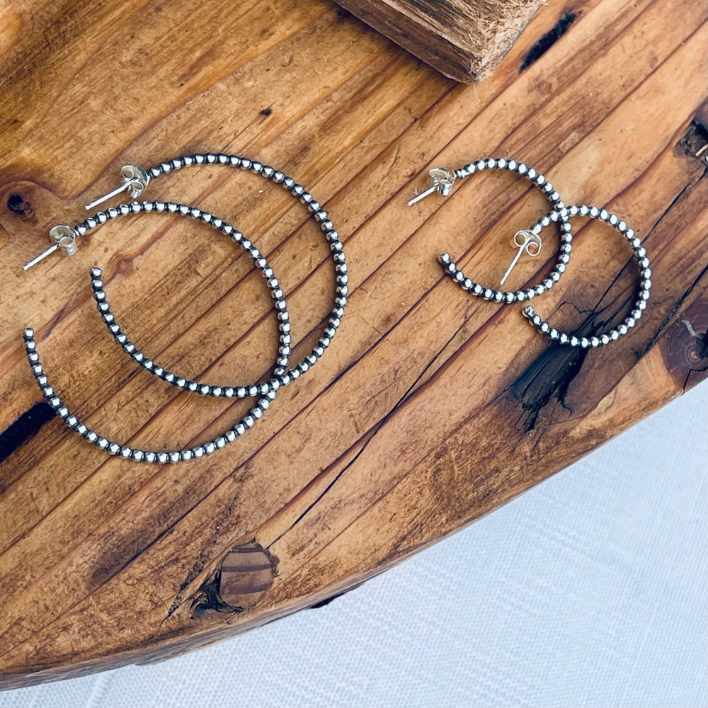 Sterling silver bead hoop earrings in small, medium, and large sizes displayed on a rustic wooden surface.