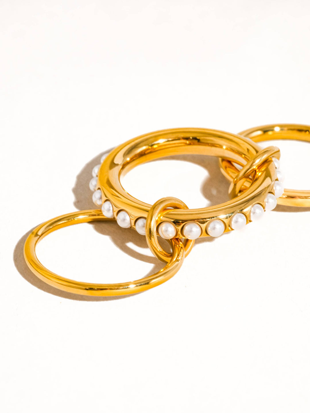 Shiny gold-tone stackable ring set with a row of white pearls along the band and interlocking hoop accents.
