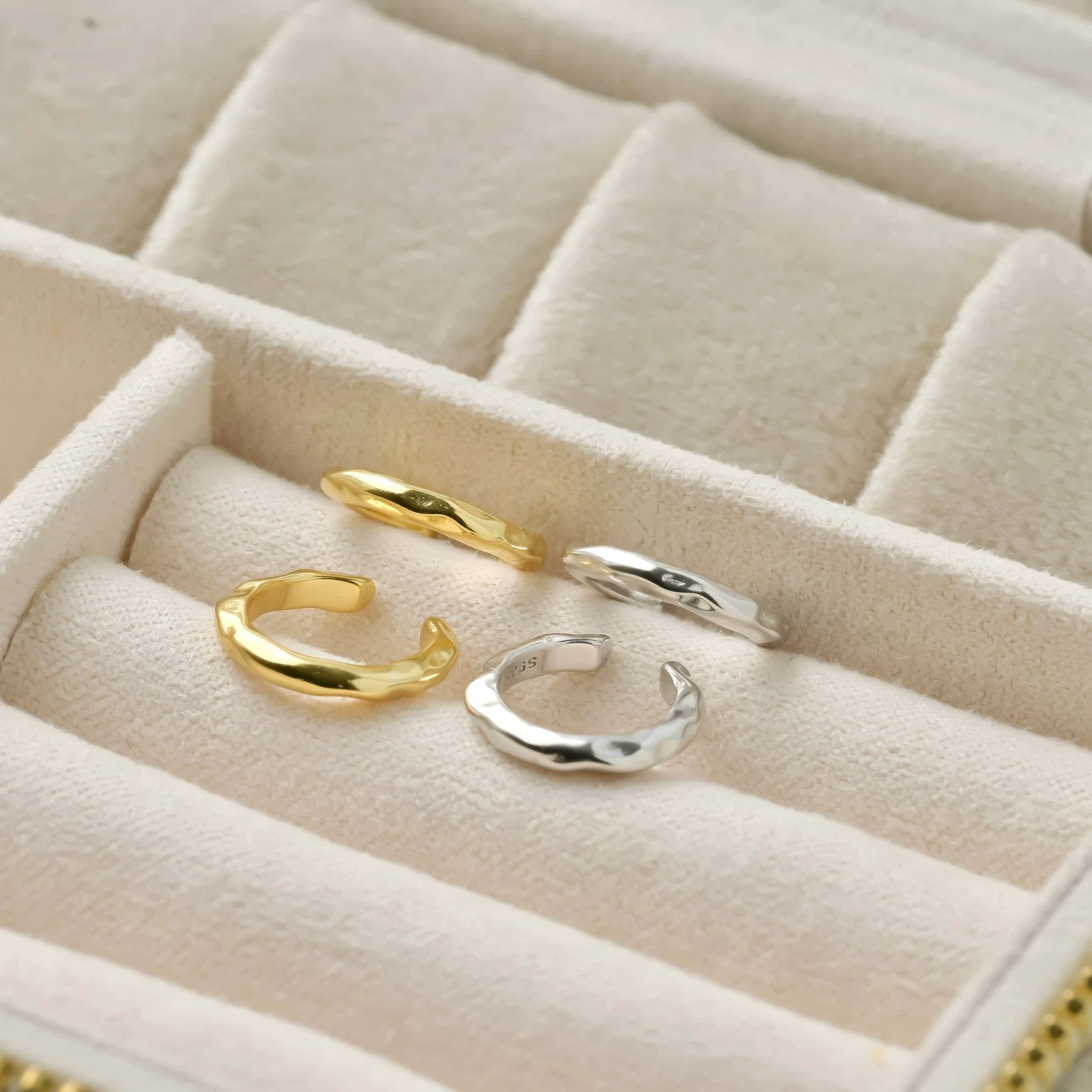 Four hammered-curb-link huggie hoops in gold and silver tones, arranged in a beige velvet jewelry tray.