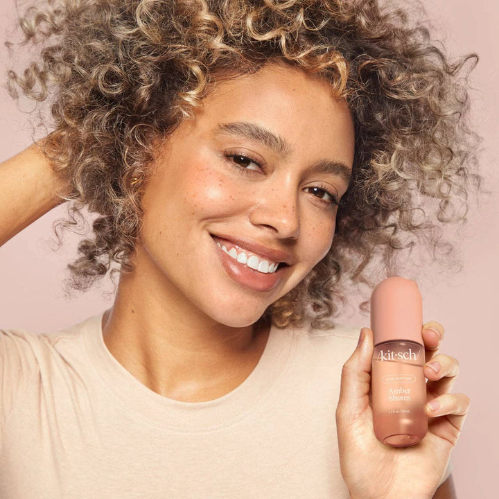 Amber Shores hair perfume by KITSCH, peachy-pink bottle held by a smiling woman