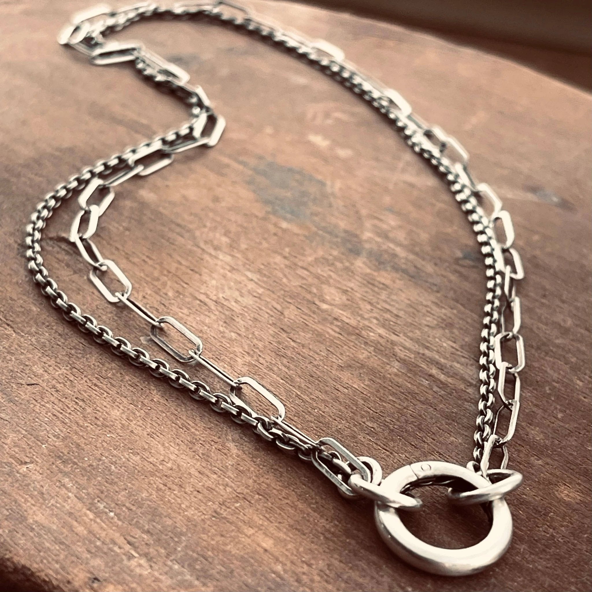 Sterling silver double-chain necklace featuring paperclip and cable links with circular ring clasp on a wooden surface.