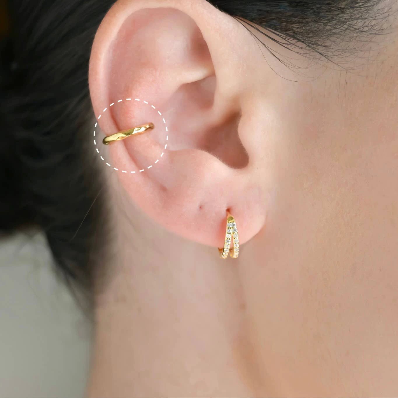 Gold curb-link ear cuff on the helix paired with a diamond-studded double-curve huggie on the earlobe.
