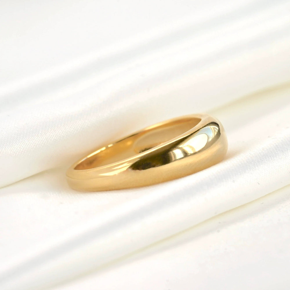 Shiny 18k gold dome ring with a thick, smooth curved band resting on white satin fabric