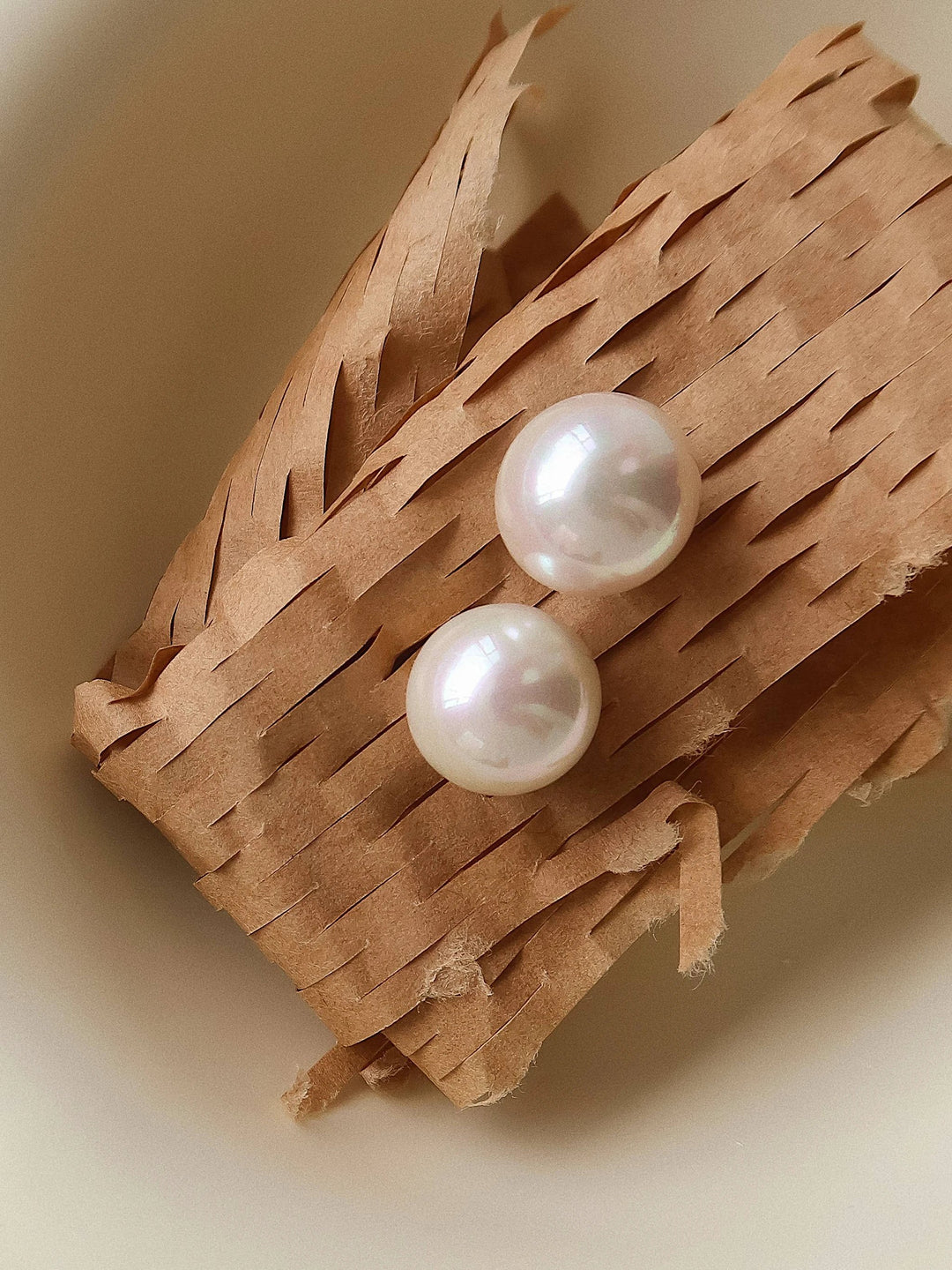 Pearl stud earrings; two white pearls on a textured brown backdrop.