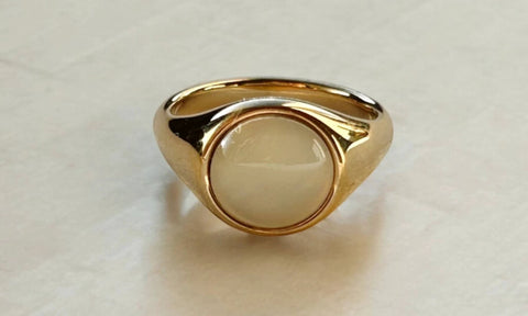 Bold gold ring with a round white cabochon bezel-set center and a chunky, high-polish band.