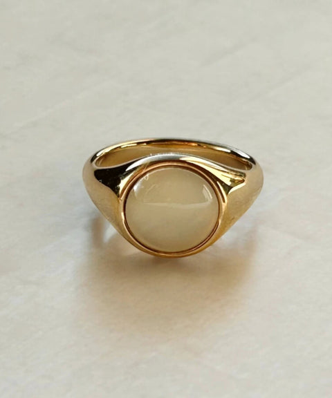 Bold gold ring with a round white cabochon bezel-set center and a chunky, high-polish band.