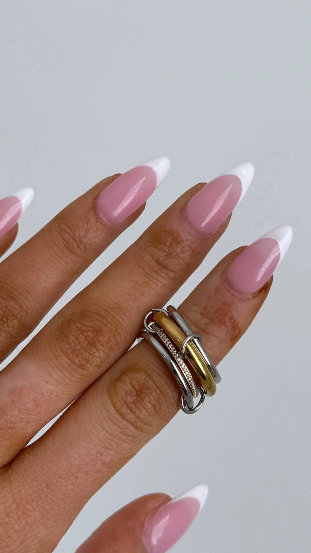 Stacked silver and gold rings with a pavé diamond band on a finger with pink-and-white nails.