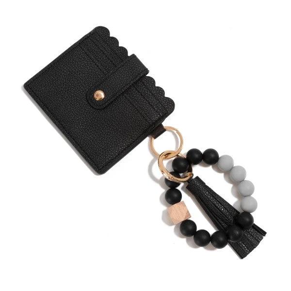 Black pebbled vegan-leather wallet with scalloped edge, attached to a gold-tone ring beaded bracelet (black and gray beads) with tassel