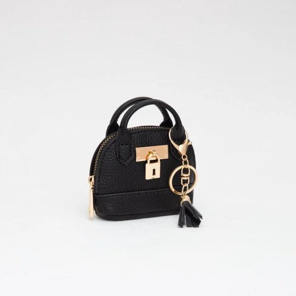 Small black vegan-leather mini purse with gold zipper, gold lock, two top handles, and a tassel charm on a gold ring.