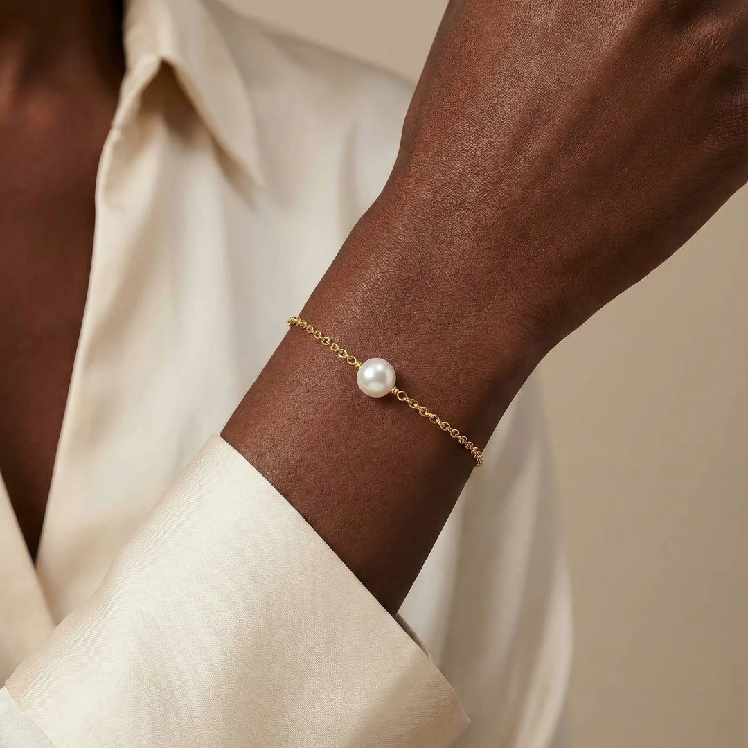 Delicate 18K gold-plated stainless steel chain bracelet with a single white pearl, worn on a dark-skinned wrist.