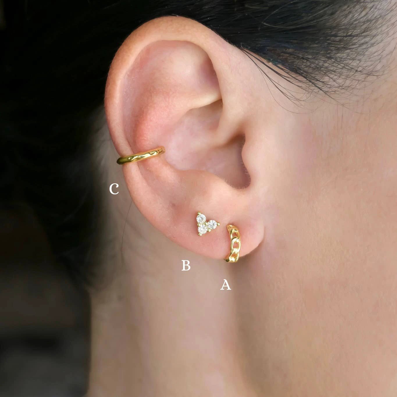 Gold curb-link huggie on the earlobe, diamond triangle stud, and gold curb-link cartilage cuff.