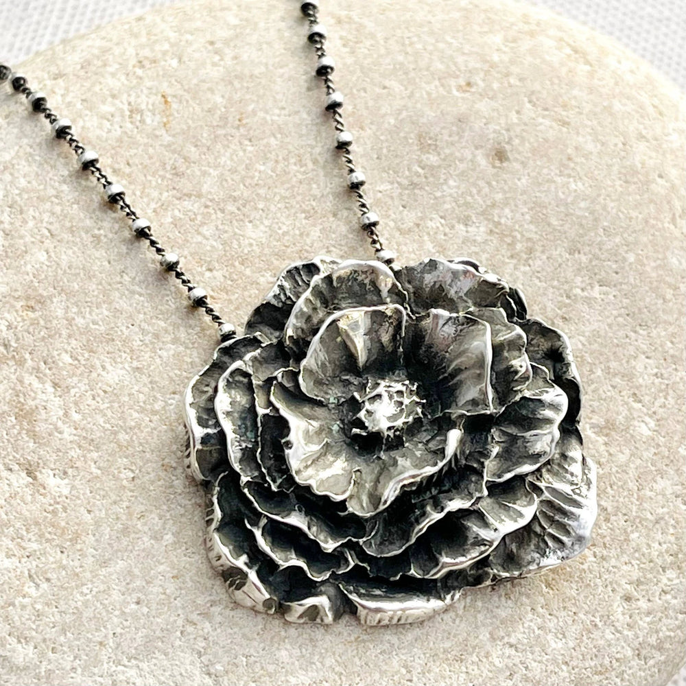 Sterling silver peony pendant with layered, textured petals and oxidized shadows on a beaded ball-chain necklace.