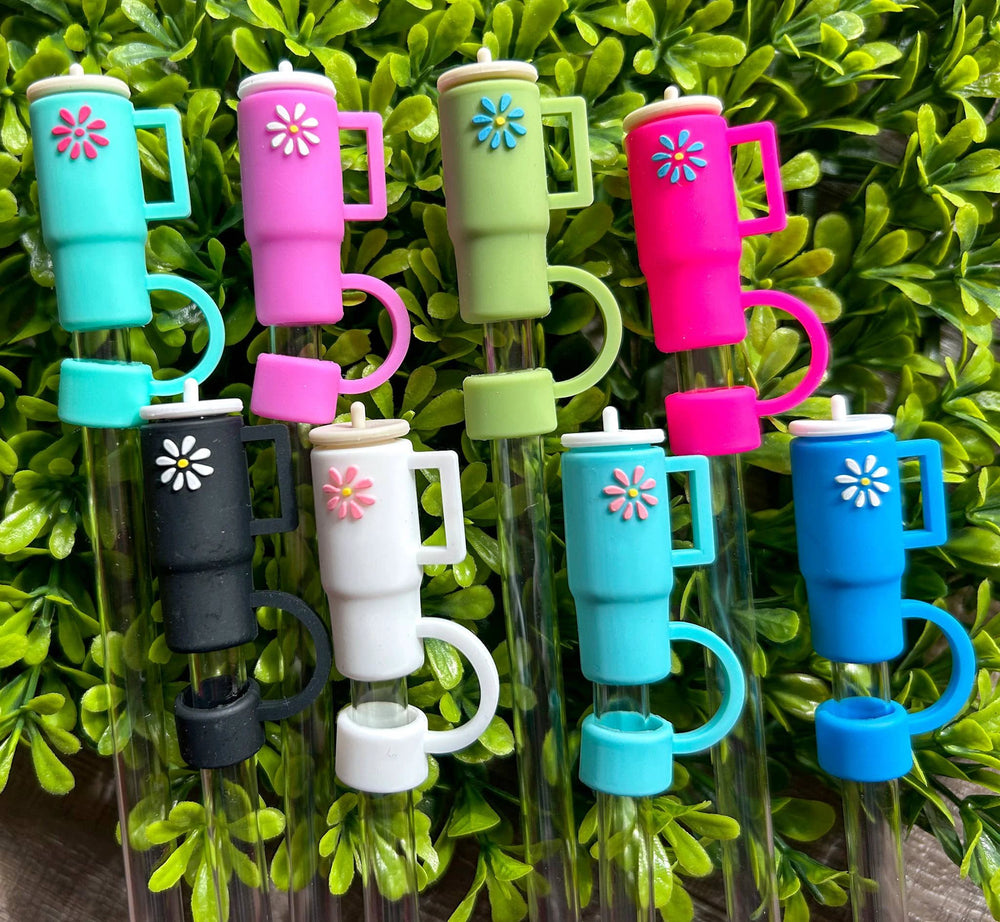 Set of eight colorful silicone daisy-topped tumbler toppers with handles in turquoise, pink, green, black, white, blue.
