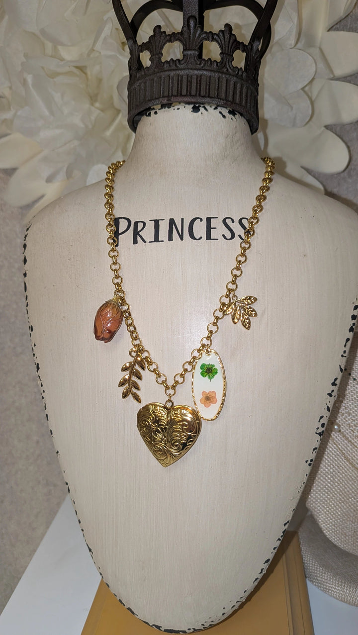 Necklace with gold-tone chain featuring a vintage heart locket, enamel floral oval, peach gemstone pendant, and two gold leaf charms.