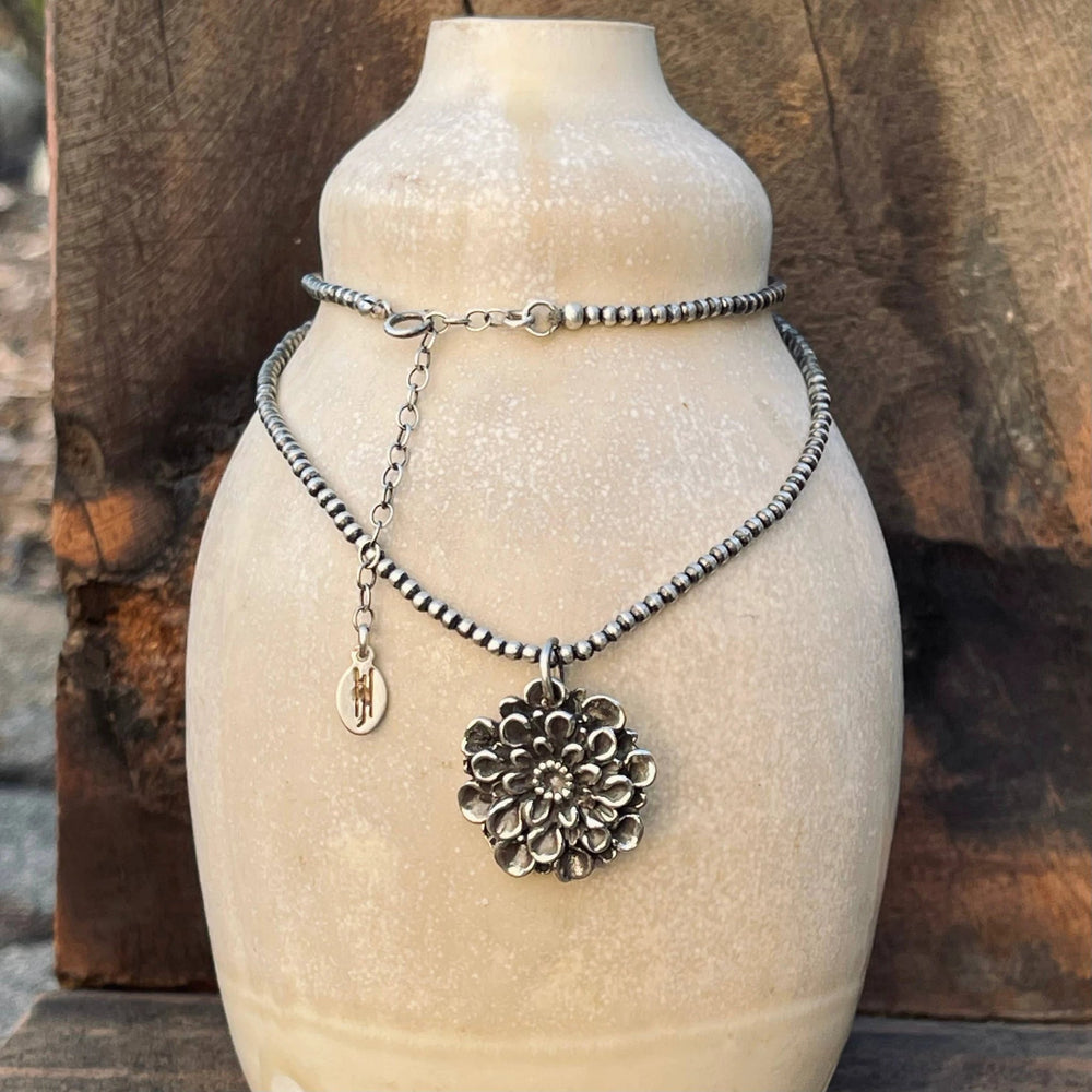 Silver beaded two-layer Dahlia necklace on a cream bust, with a large flower pendant and a tiny oval charm.