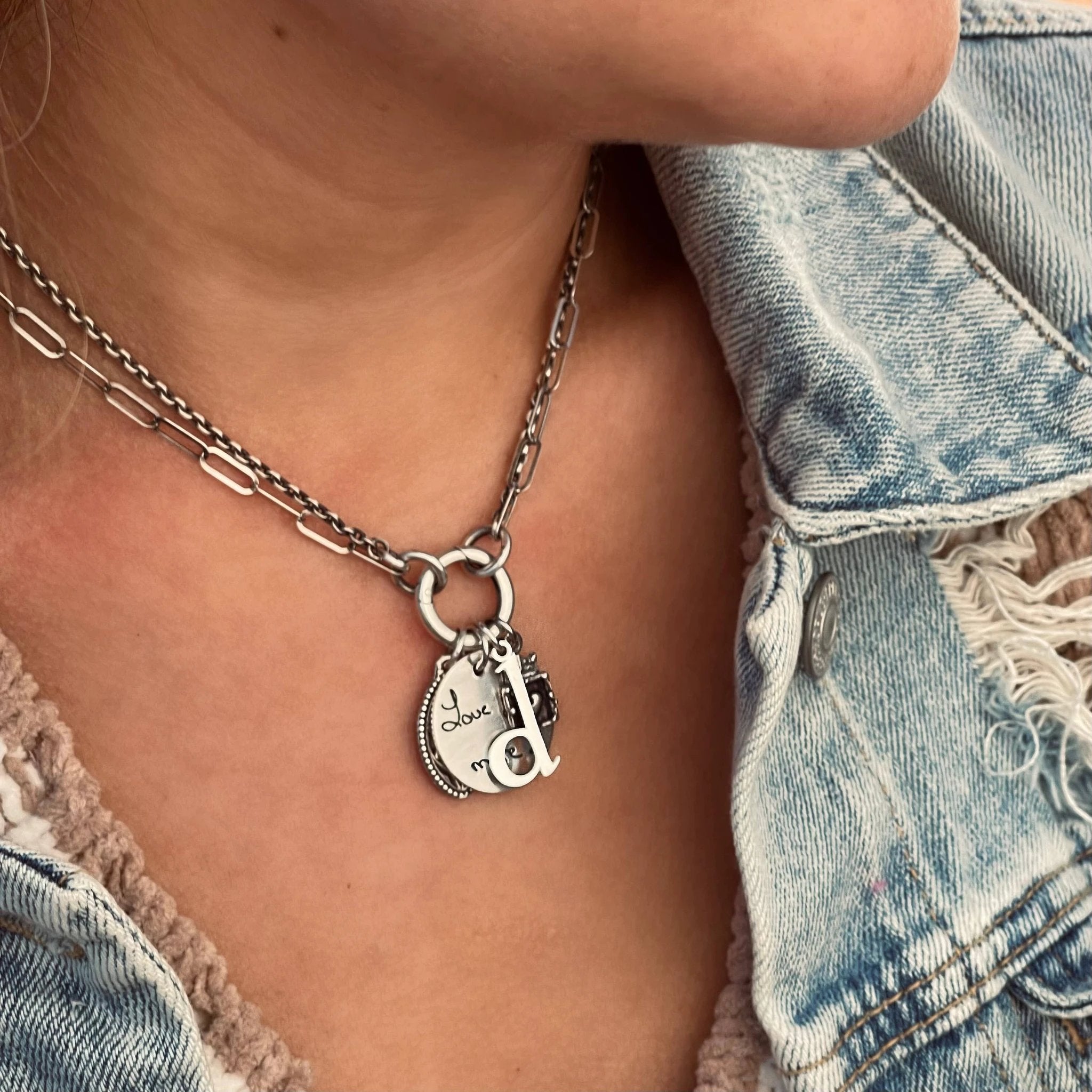 Double sterling silver charm chain with circular pendant cluster and coin charms, engraved Love, worn over a denim jacket