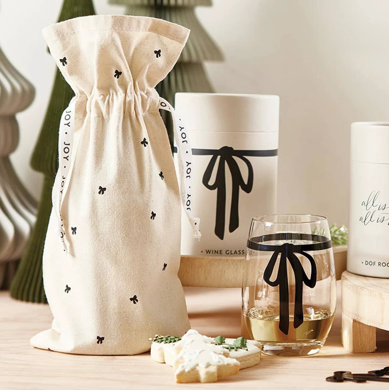 Clear stemless wine glass with a black bow around the middle, beside a beige drawstring pouch printed with tiny bows.
