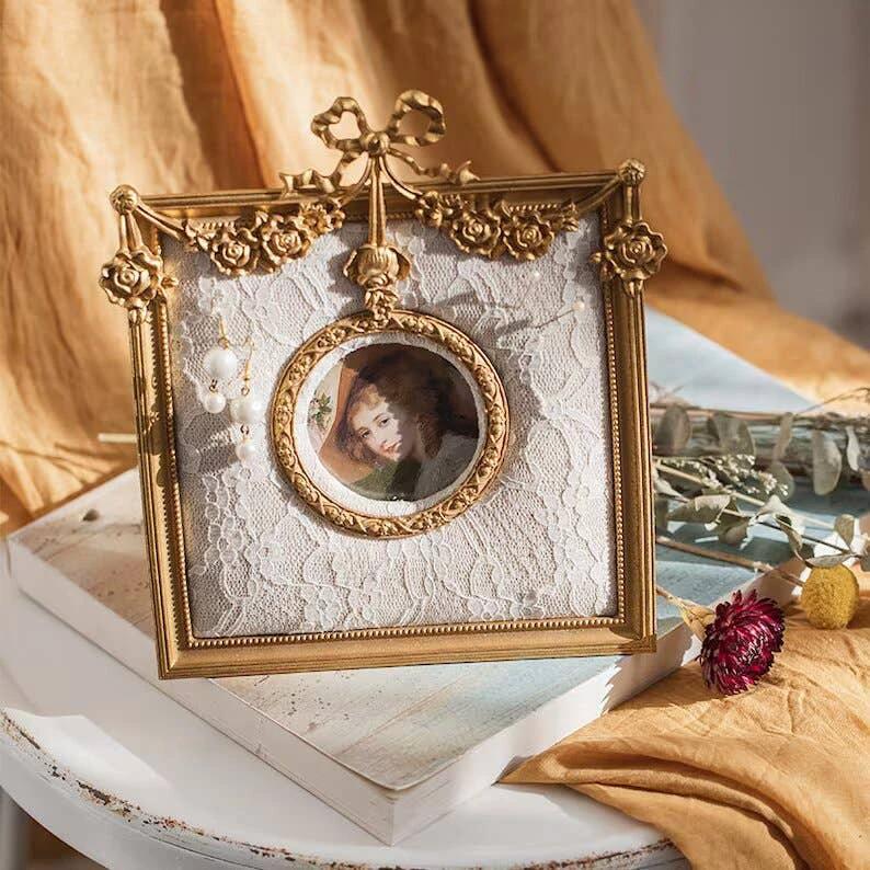 Ornate gold vintage photo frame with lace backing, circular cameo portrait at center, floral corners and a bow top.