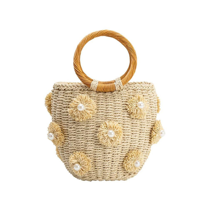Beige woven straw tote with a circular braided handle and added flower-shaped rosettes each with a pearl center.