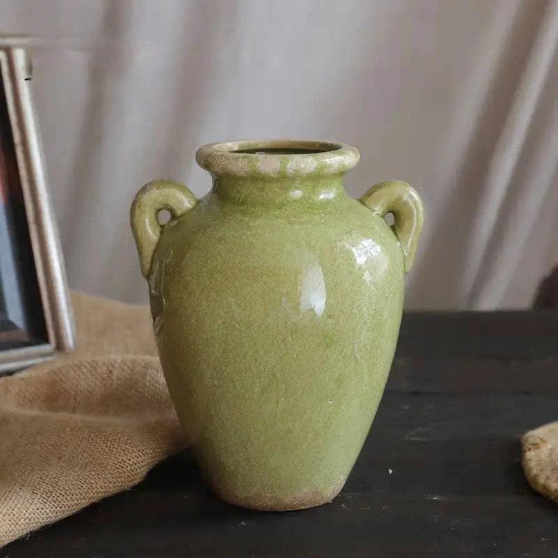 Green glazed ceramic vase with a rounded body, short neck, and twin loop handles on the sides.