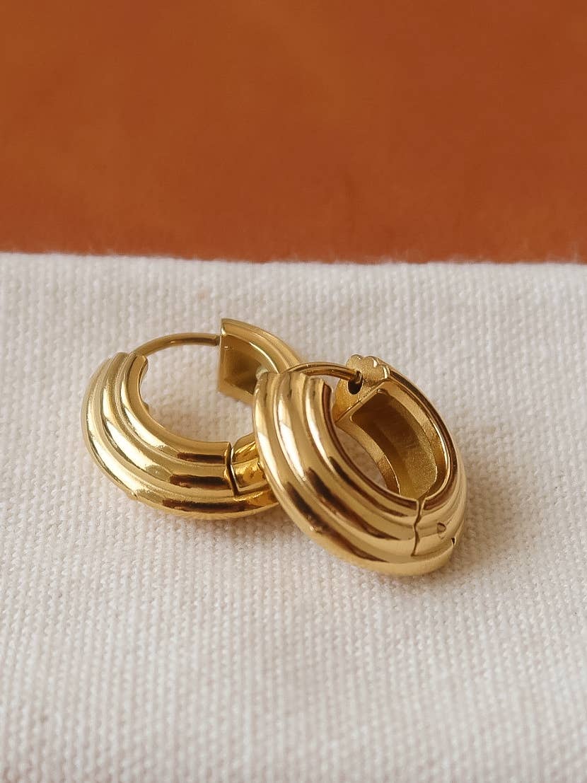 Pair of thick gold hoop earrings with three ridged bands and hinged clasps on white fabric