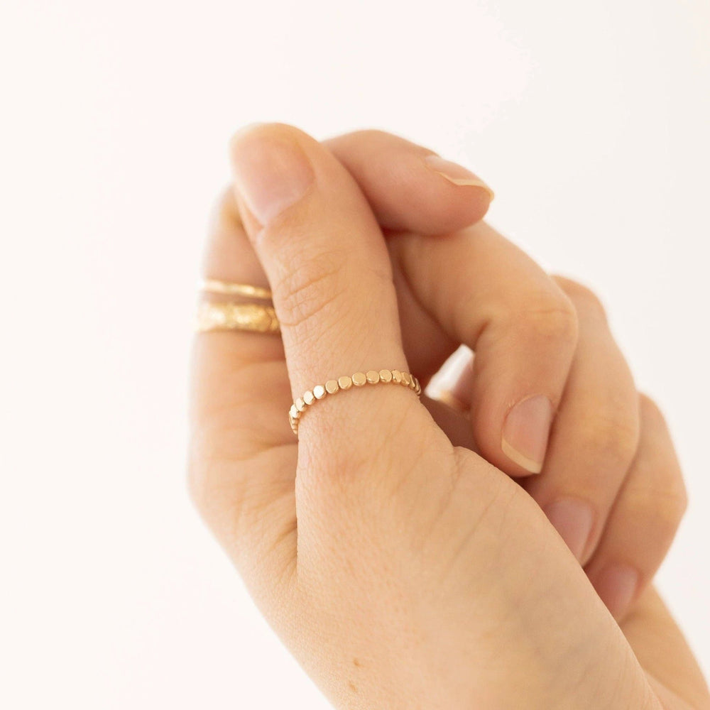 Close-up of a hand wearing a dainty gold beaded ring on one finger, with a textured gold band on the adjacent finger.