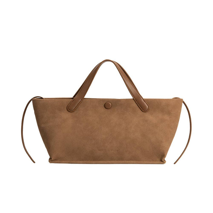 Tan suede tote with two short handles, center snap closure, and long side tie straps on a trapezoid silhouette.