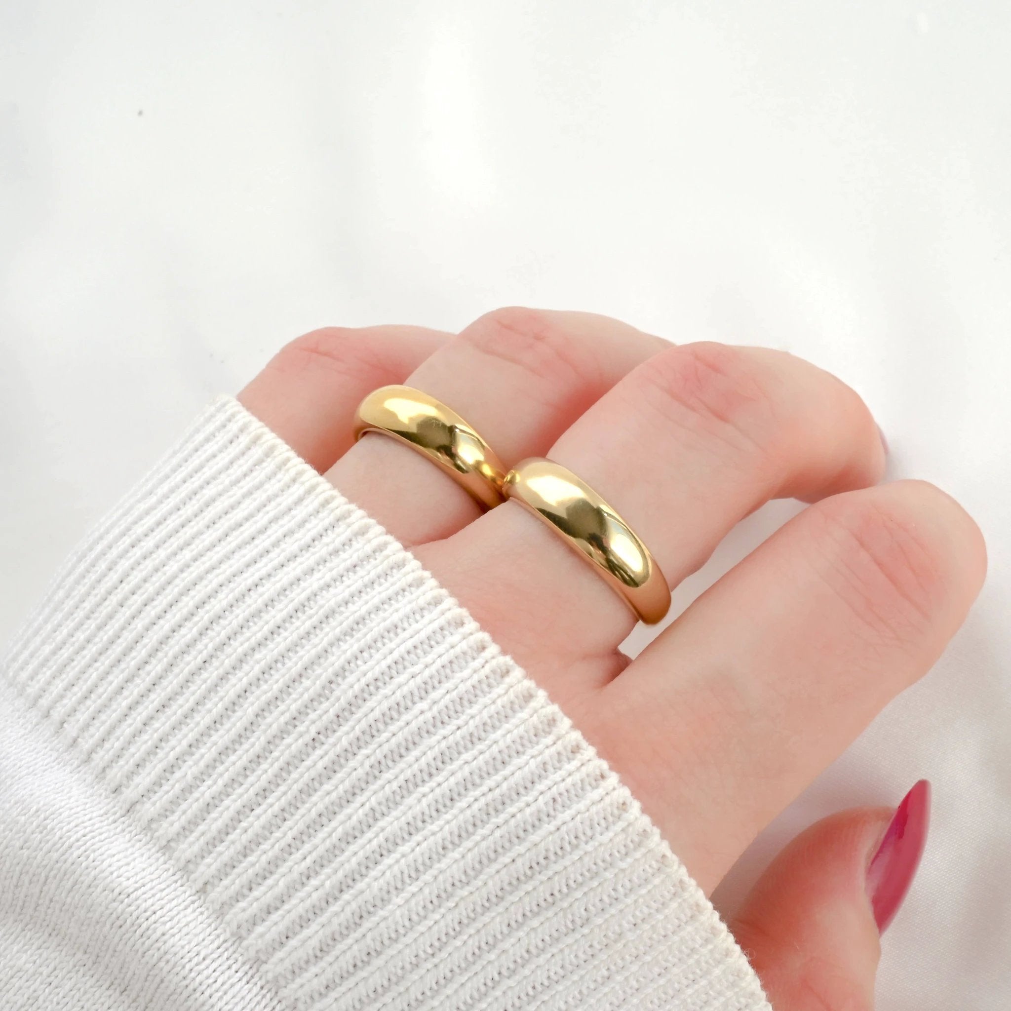 Two thick, glossy 18k gold dome rings stacked on a finger, white ribbed sleeve visible.