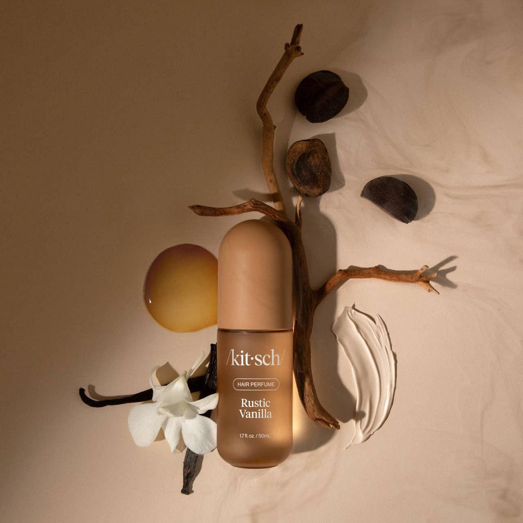 Rustic Vanilla hair perfume bottle by KITSCH; beige gradient bottle with gold cap, surrounded by natural decor.