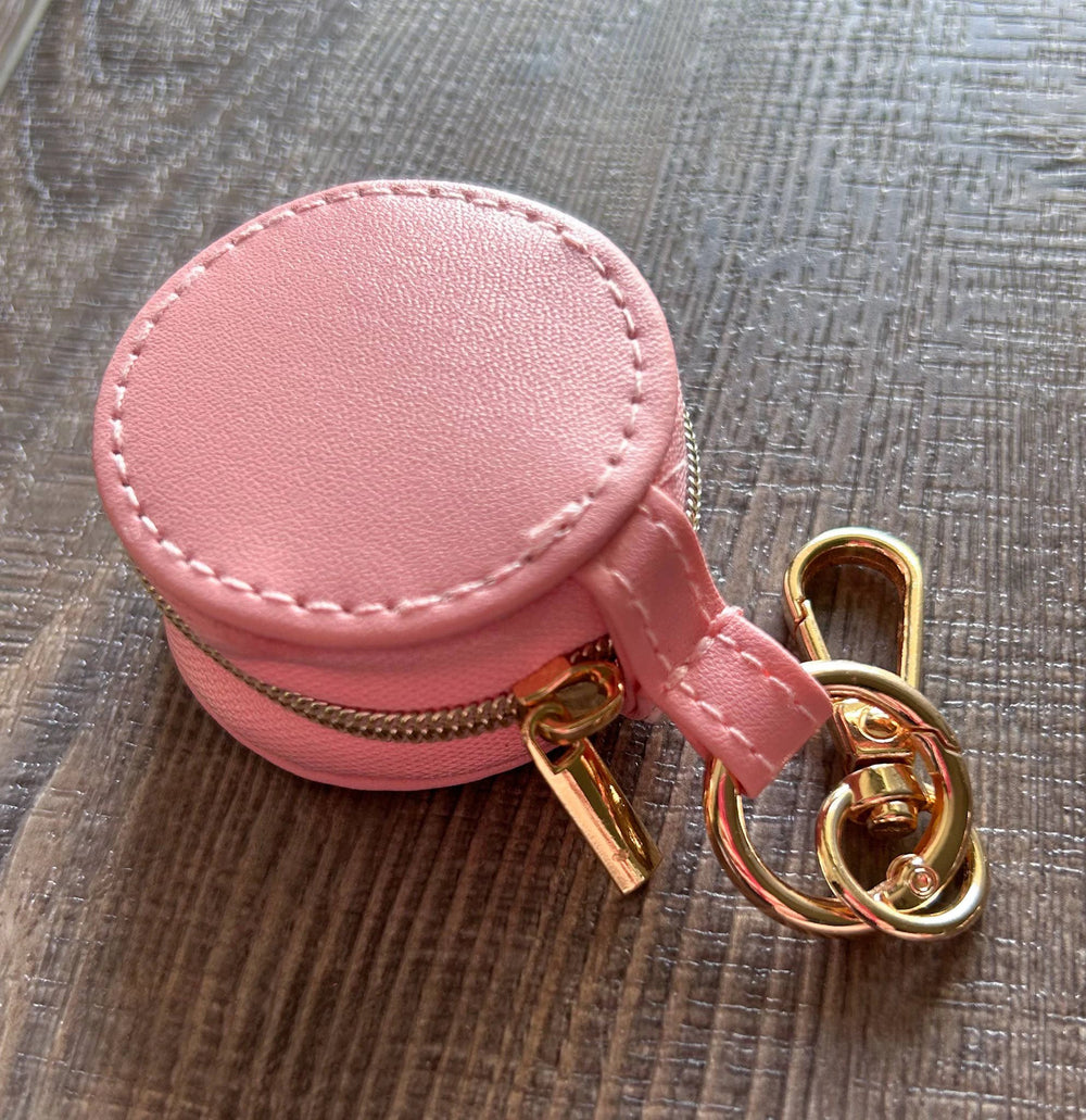 Round pink faux-leather jewelry holder with a gold zipper, small strap, and gold keychain rings.