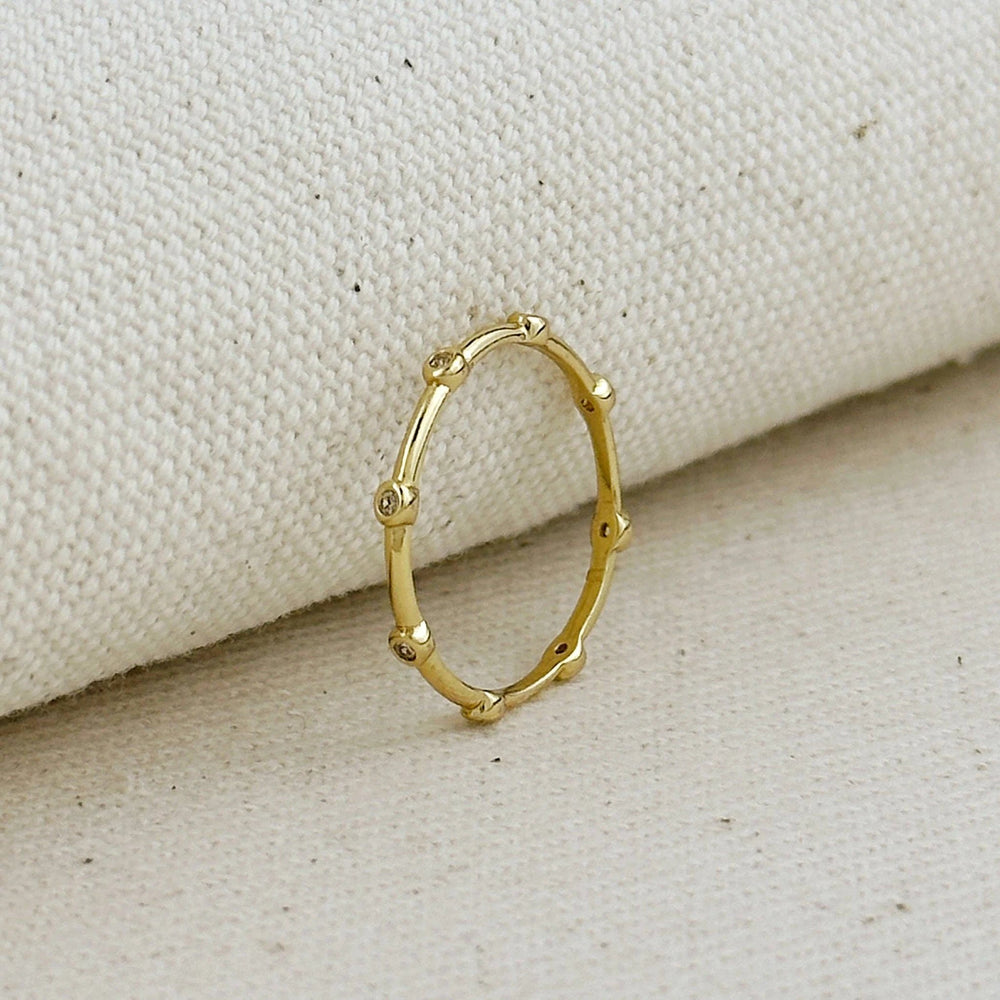 Gold-filled ring with small cubic zirconia stones set as dots around a slim circular band, on beige fabric.