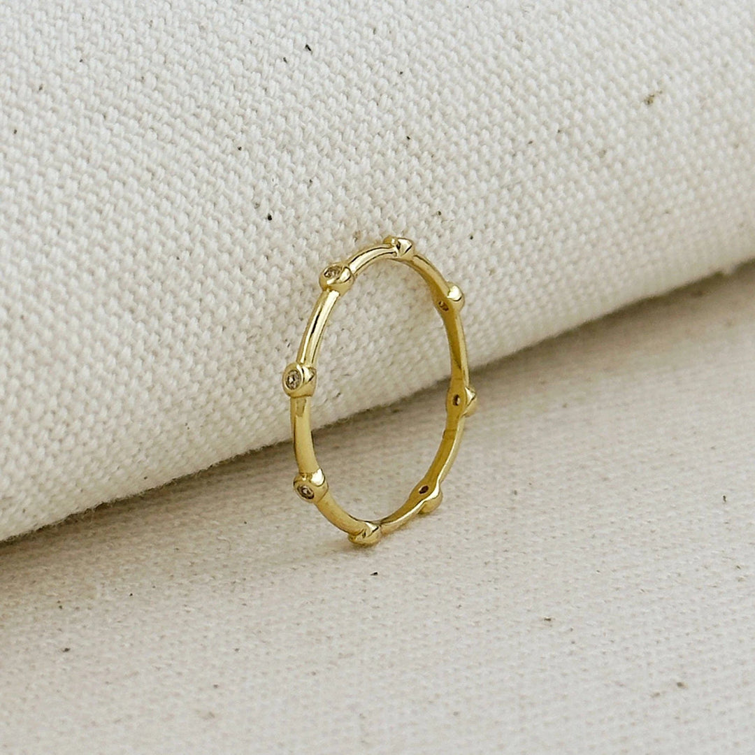 Gold-filled ring with small cubic zirconia stones set as dots around a slim circular band, on beige fabric.