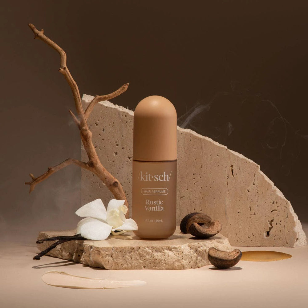 KITSCH Rustic Vanilla Hair Perfume bottle in warm beige with rounded cap, set on a stone slab with branches