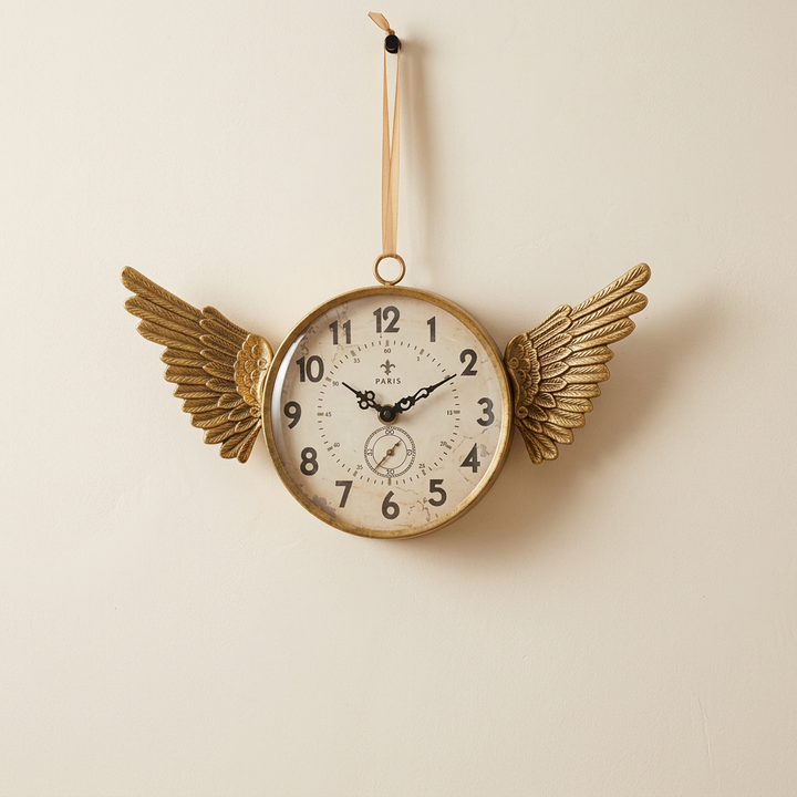 Gold angel wing wall clock against a clean ivory wall