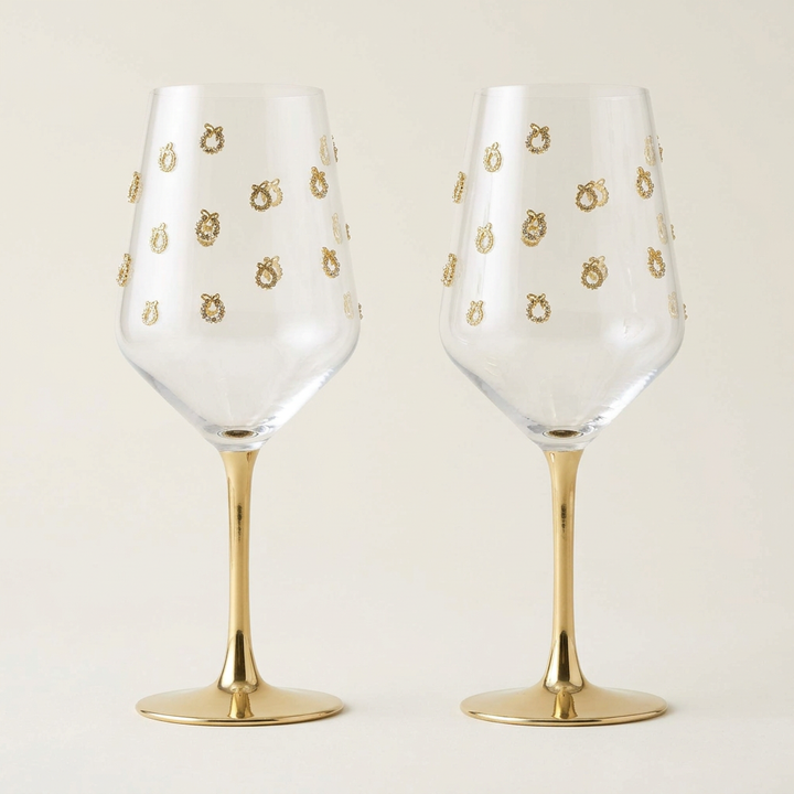 Pair of empty gold wreath wine glasses on a plain ivory background