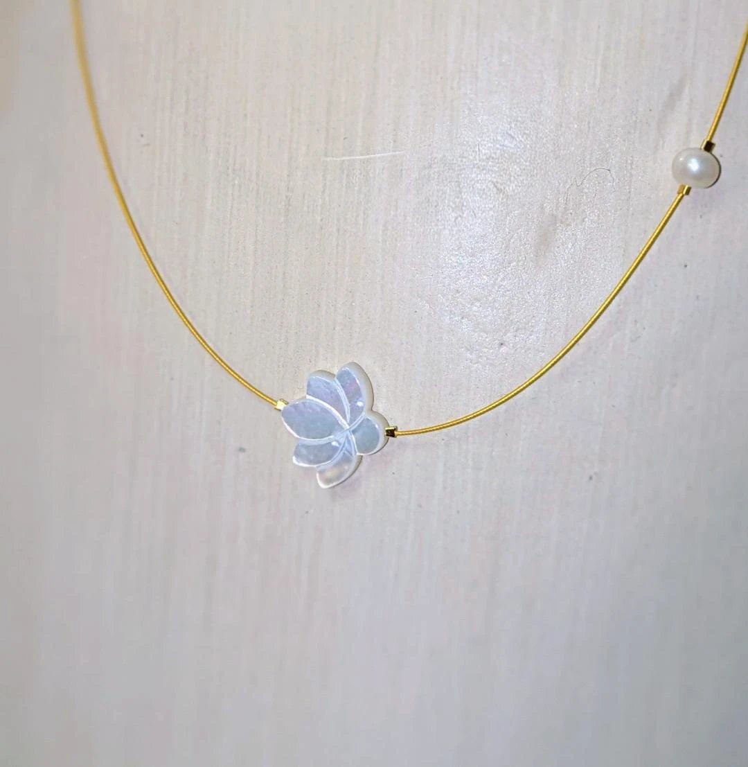 The White Lotus Necklace: gold-tone cord with a white lotus flower pendant and pearl bead accents.