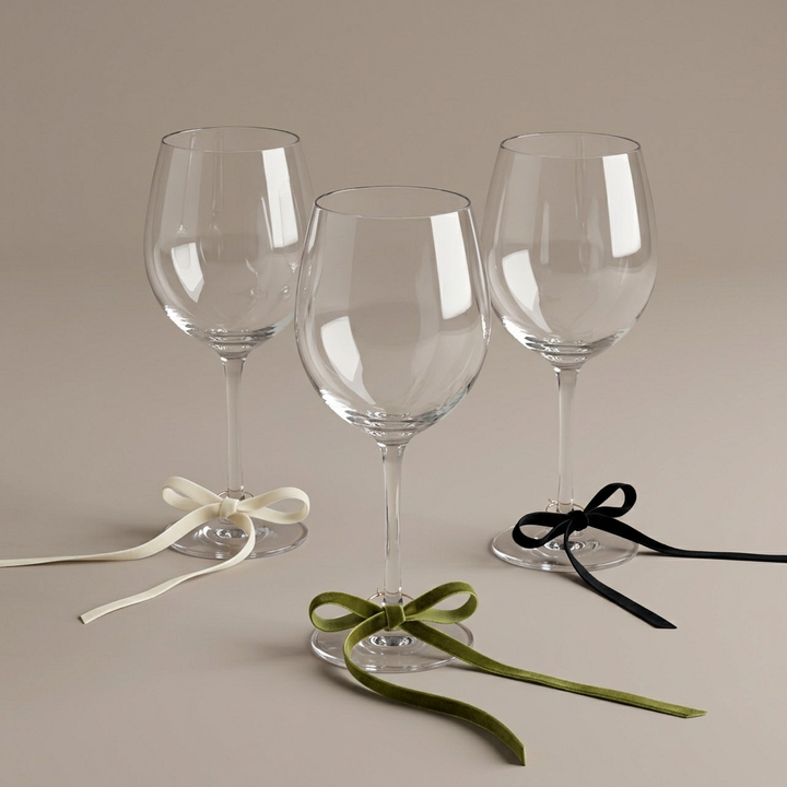 Velvet bow wine charms styled on glass stems against a plain warm greige background